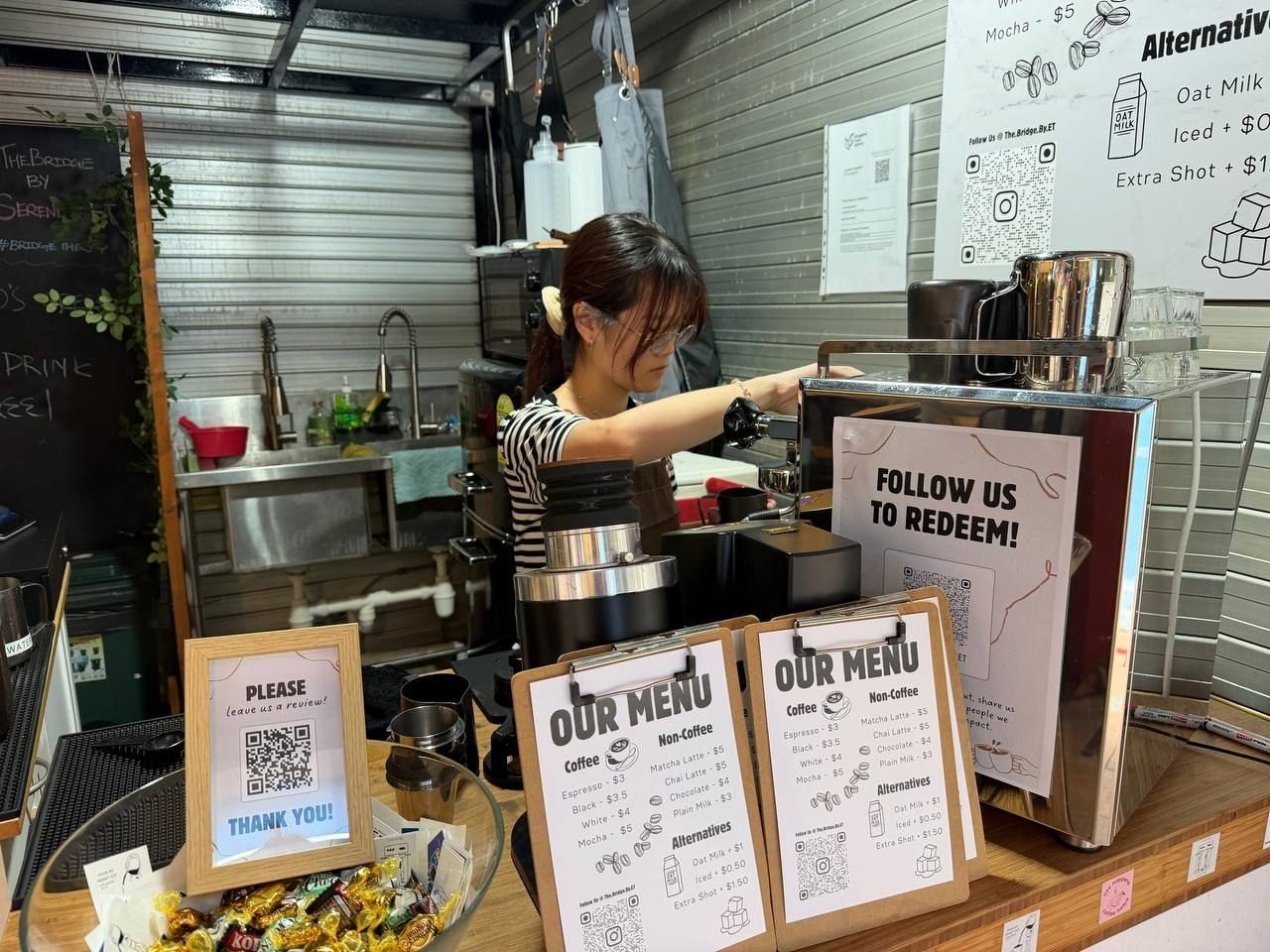 Behind the counter: our barista at the espresso machine beside the Follow Us to Redeem challenge sign